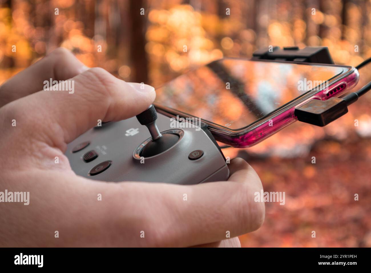 Kharkiv, Ukraine - 15. Oktober 2021: DJI Drohnen-Fernbedienung in Händen mit vernetztem Telefon Nahaufnahme im Herbst lebendiger Wald unscharfer Hintergrund Stockfoto