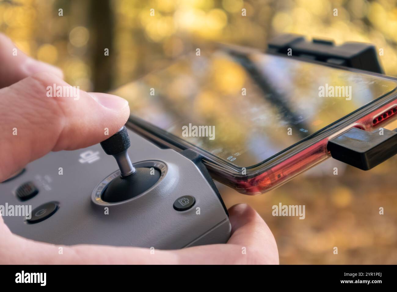 Charkiv, Ukraine - 15. Oktober 2021: DJI Drohnen-Fernbedienung in Händen mit angeschlossenem Telefon. Nahaufnahme der Drohne im herbstlichen goldenen Wald Stockfoto