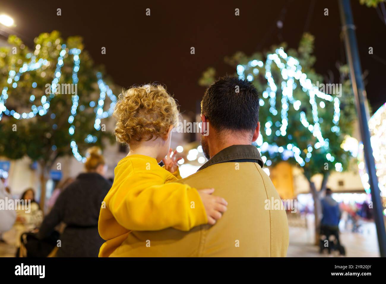 Vater und Kind beobachten bei Nacht auf einem festlichen Stadtplatz weihnachtslichter und feiern die Weihnachtszeit mit Liebe und Zweisamkeit Stockfoto