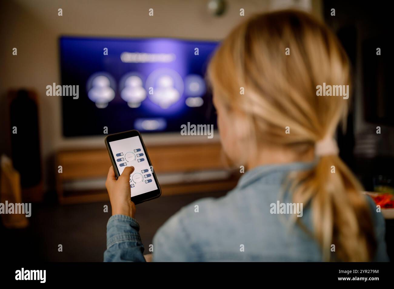 Rückansicht des Jungen mit Smartphone als Fernbedienung für das Fernsehen zu Hause Stockfoto