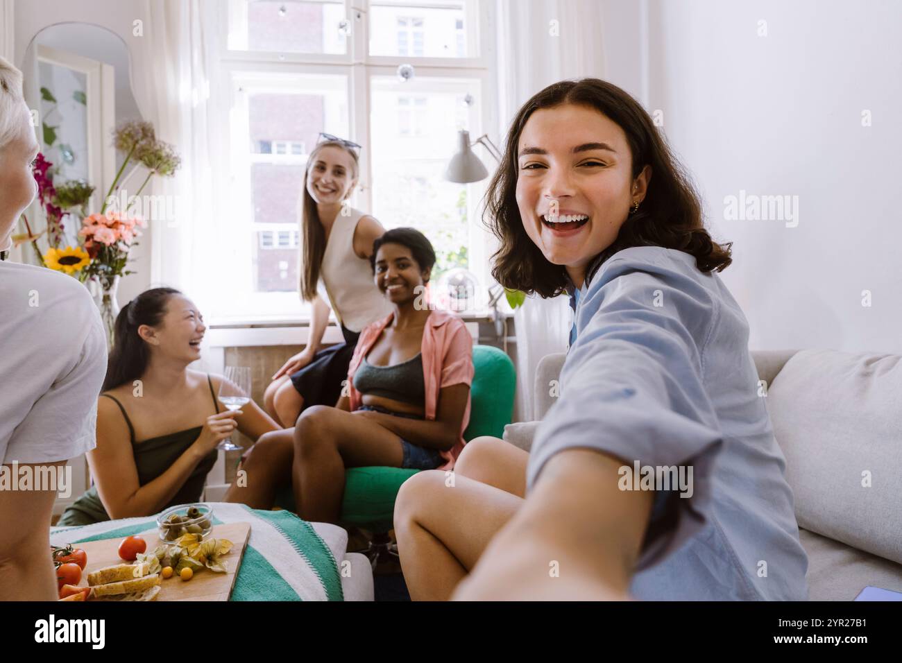 Porträt einer glücklichen Frau, die Selfie mit Freunden macht, die zu Hause sitzen Stockfoto