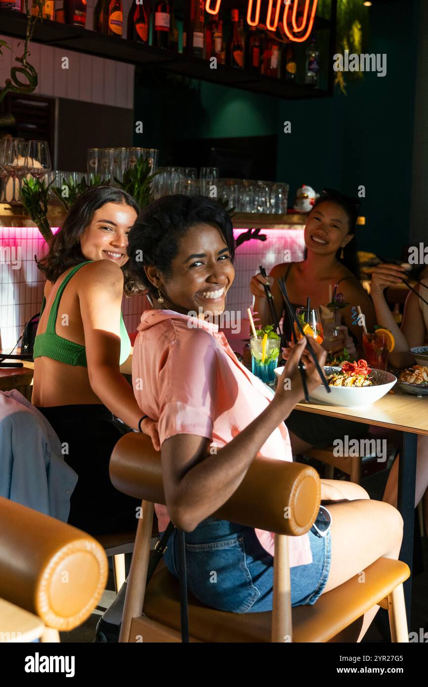 Seitenansicht Porträt einer lächelnden Frau, die über die Schulter schaut, während sie mit weiblichen Freunden im Restaurant essen Stockfoto