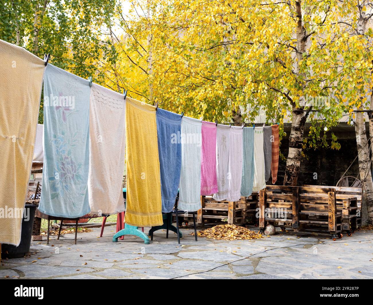 Viele bunte Handtücher hängen in der Herbstsaison Wäsche auf der Wäscheleine im Außenbereich. Wäscheleine mit frisch gewaschener Kleidung im Freien zu Hause Stockfoto