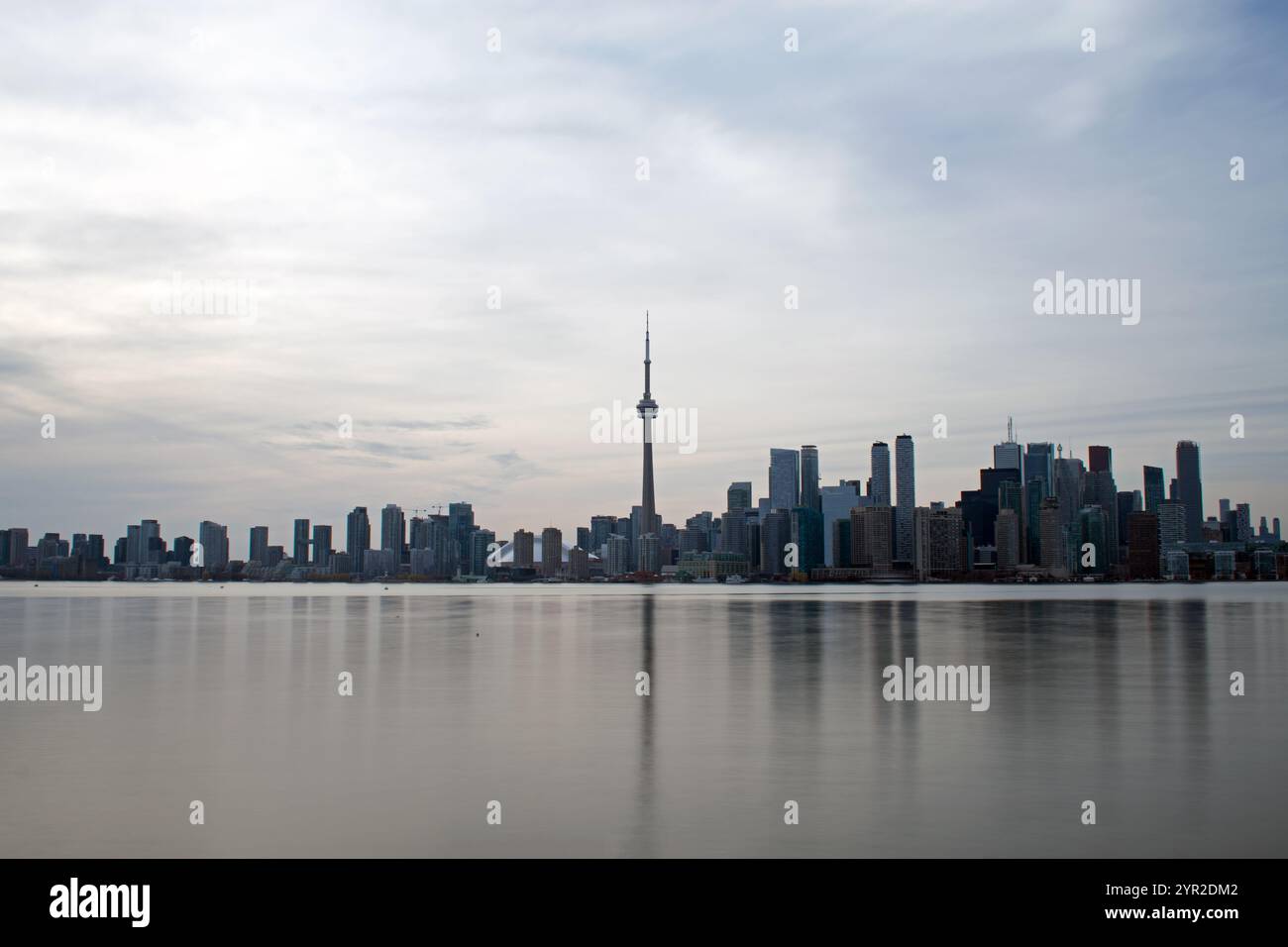Das glatte Wasser des Lake Ontario spiegelt die beeindruckende Skyline von Toronto wider. Ein grauer Tag mit minimalistischem Himmel und strahlenden Lichtwolken. Ontario, Kanada. Stockfoto