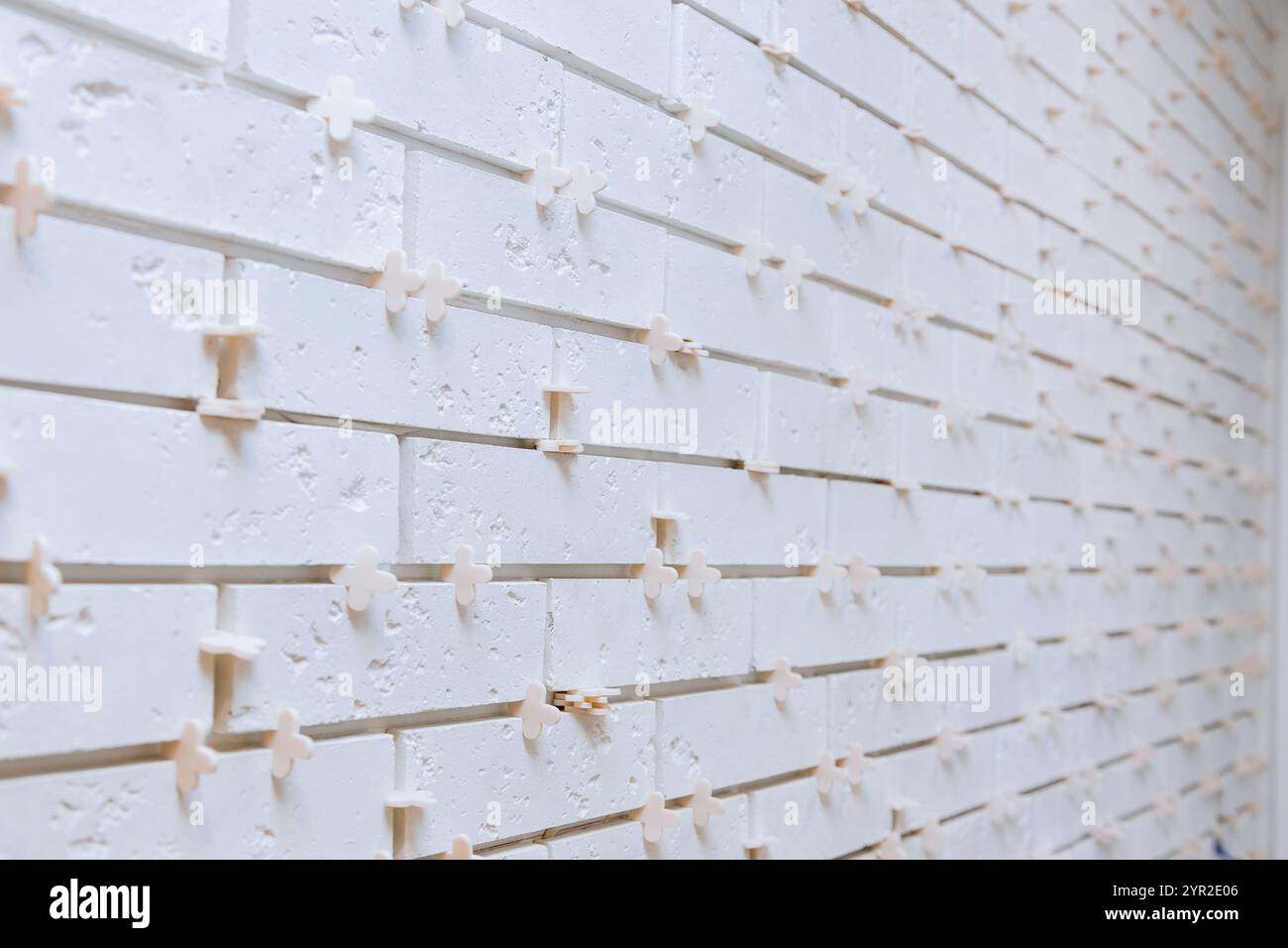 Eine weiße Wand wird für die Oberflächenbearbeitung vorbereitet, mit gleichmäßig abgesetzten Holzabstandshaltern vor einem hellen Hintergrund, die ein minimalistisches Design betonen. Stockfoto