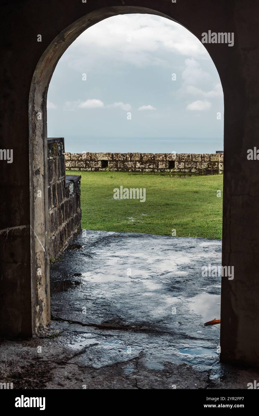 St. George's, Grenada - 4. Januar 2018: Ein Blick durch einen Bogengang in Fort Frederick mit Blick auf den üppig grünen Rasen und das ferne Meer. Stockfoto