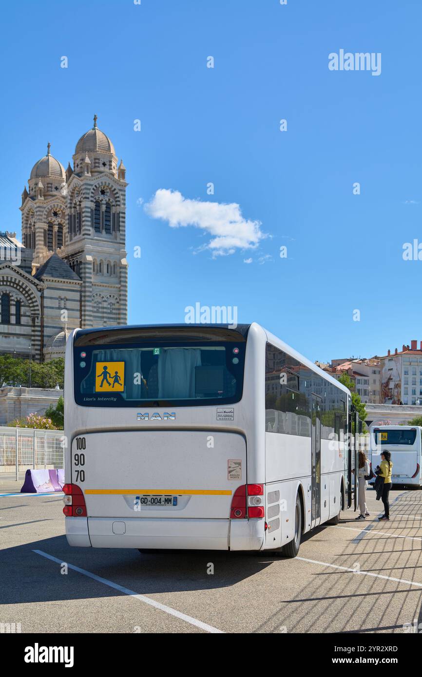 Marseille. Frankreich - 02. Dezember 2024: Das Bild zeigt einen weißen Überlandbus, der vor einer historischen Kathedrale in Marseille geparkt ist und die Tiere erfasst Stockfoto