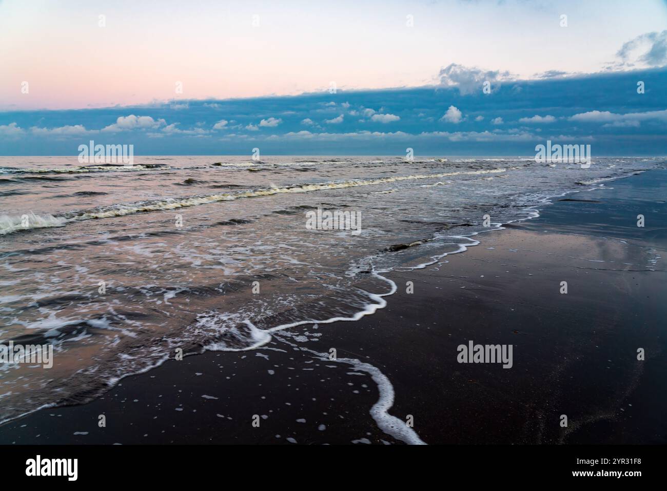 Sandstrand am Meer nach Sonnenuntergang mit dunklen Gewitterwolken in der Ferne Stockfoto