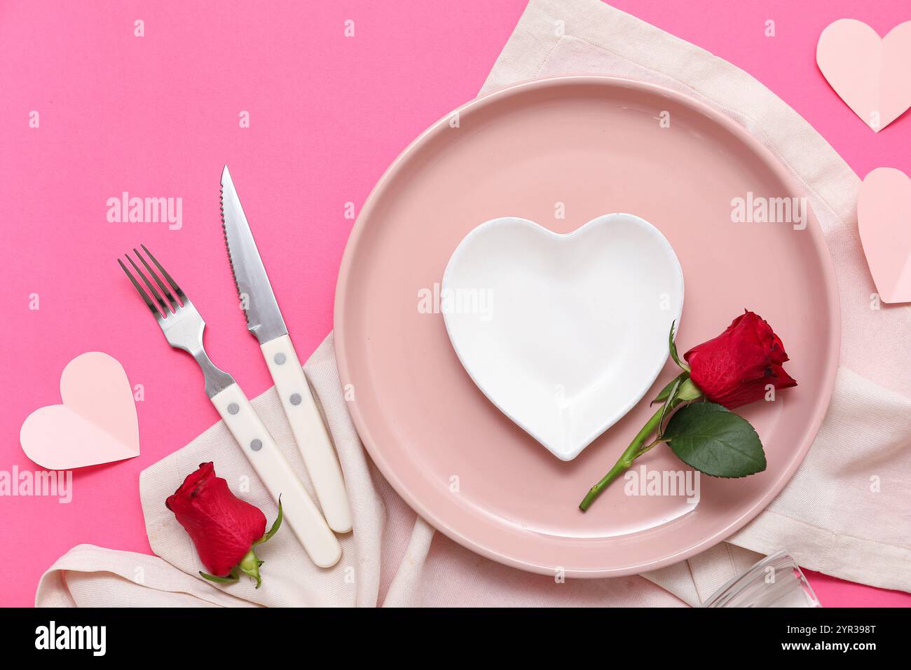 Tischeinstellung für Valentinstag mit Papierherzen, Serviette und Rosenblumen auf rosa Hintergrund Stockfoto