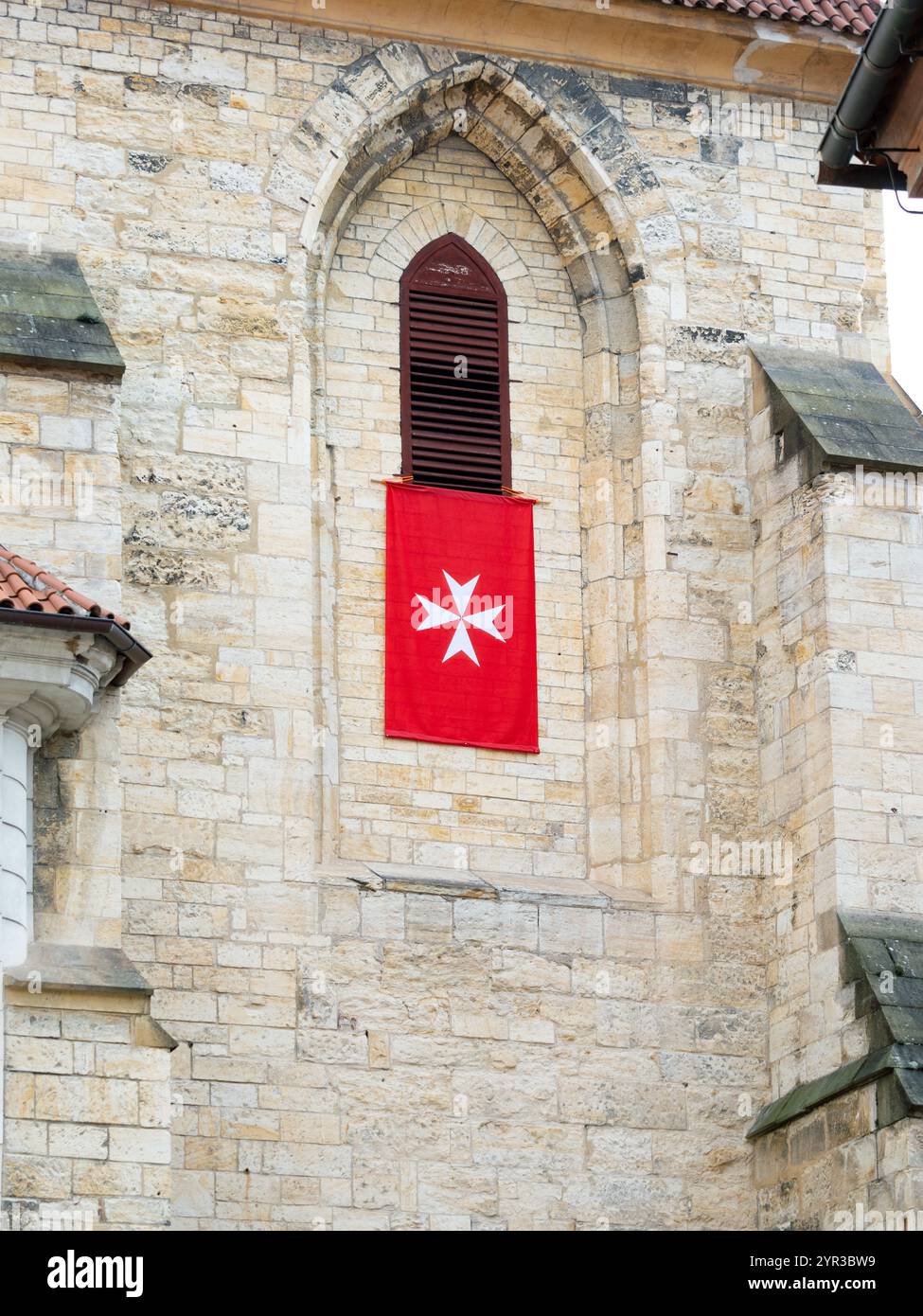 Die Flagge des Malteserordens auf einem Kirchengebäude. Ein weißes Kreuz auf rotem Hintergrund. Der Orden gehört der katholischen Kirche. Stockfoto