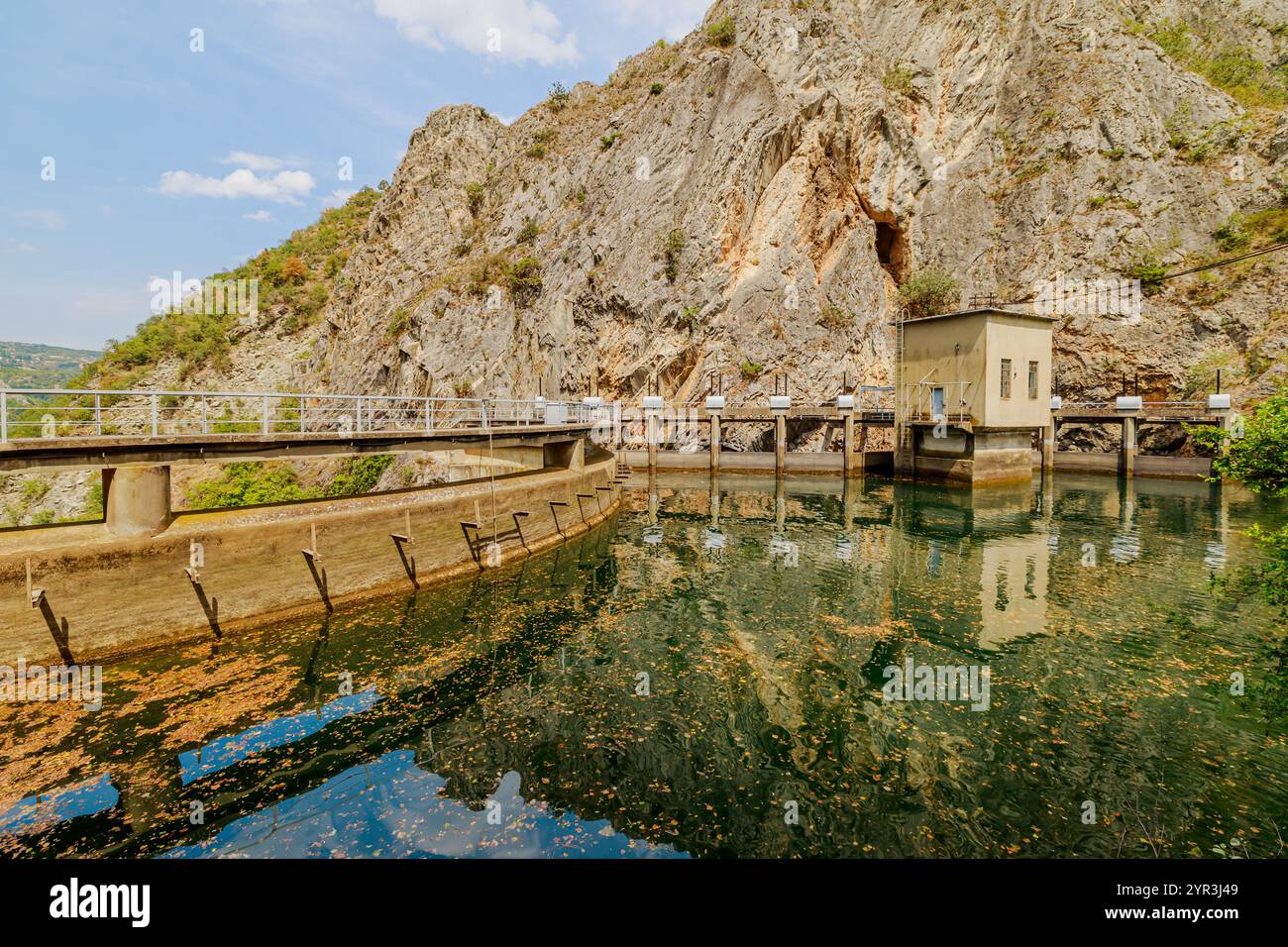 Die Betonmauer, die entlang der Canyon-Mauer kurbelt, hält das grüne Wasser des Matka-Sees zurück und bietet Wasserkraft und landschaftliche Schönheit in Mazedonien Stockfoto