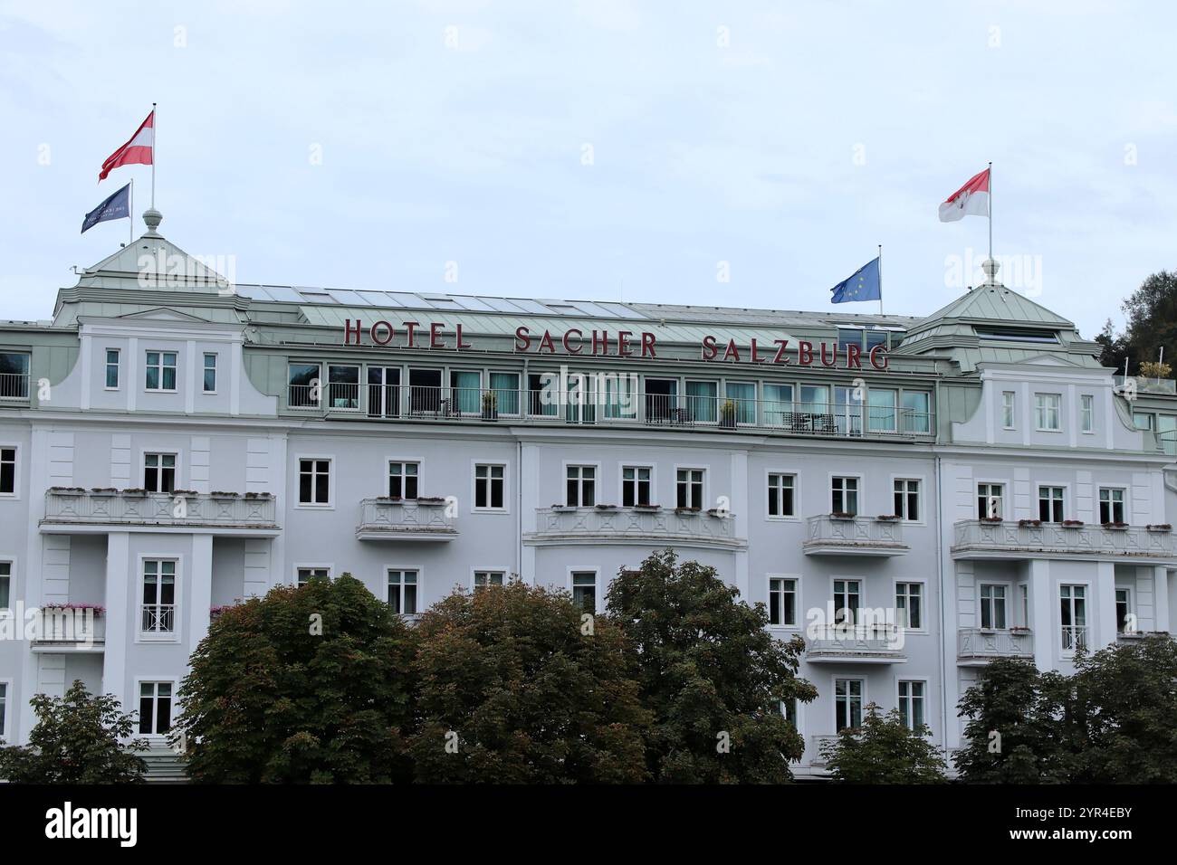 Salzburg, Österreich - 1. Oktober 2024: Elegantes Äußere des historischen Hotels Sacher Salzburg mit Fahnen, die an einem bewölkten Tag fliegen Stockfoto