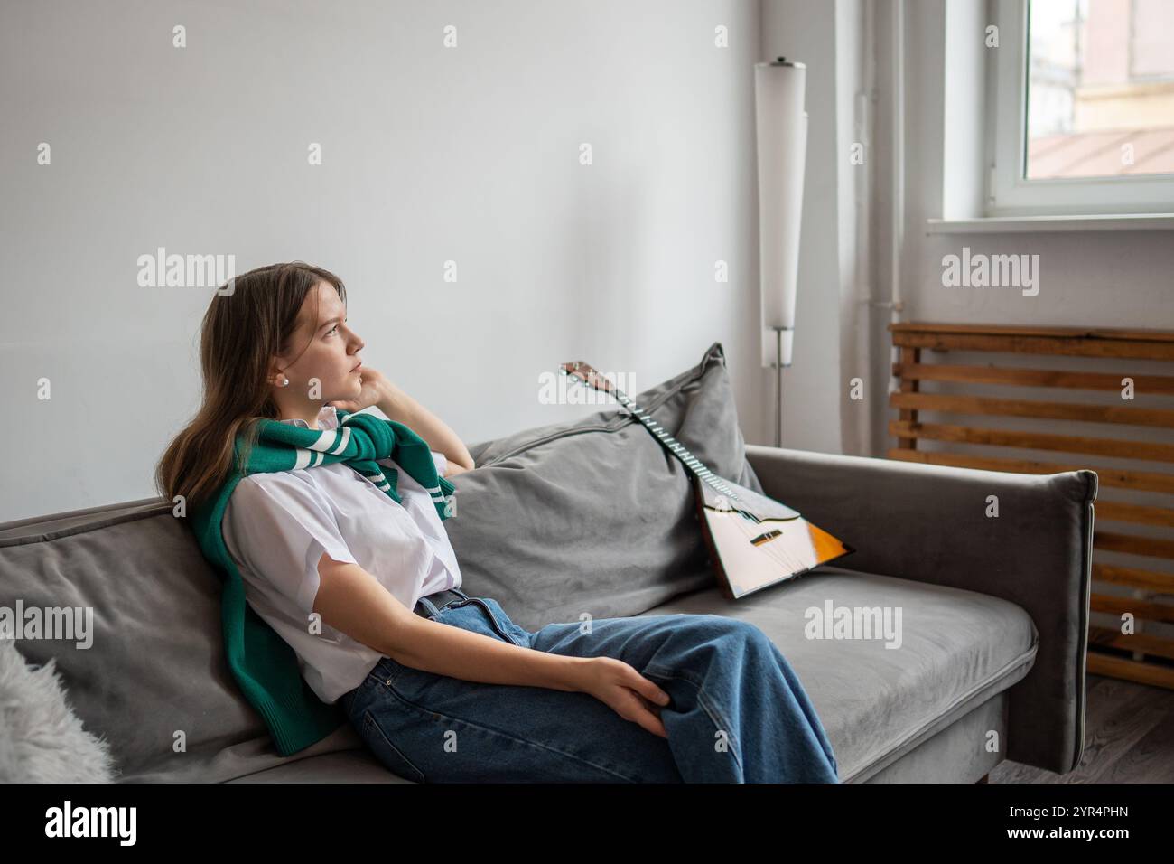 Ruhige Frau, die auf dem Sofa im Wohnzimmer nachdenkt, nachdem sie zu Hause Balalaika gespielt hat. Machen Sie Pause, ruhen Sie sich aus Stockfoto