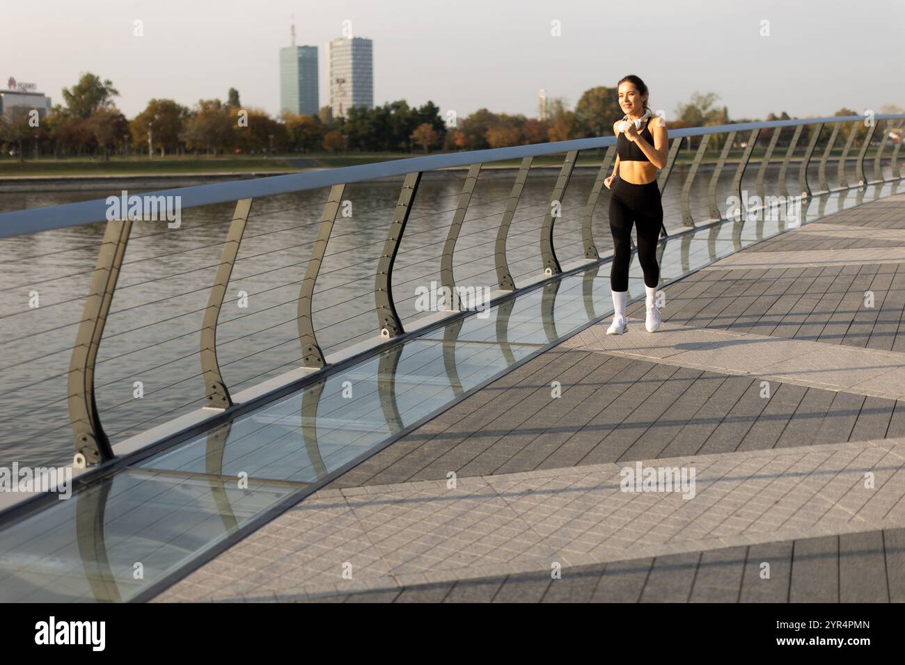 Ein Alleinläufer begrüßt die morgendliche Ruhe und joggt entlang eines wunderschönen, von Bäumen umsäumten Pfades am Wasser, während sich die Skyline der Stadt im C widerspiegelt Stockfoto