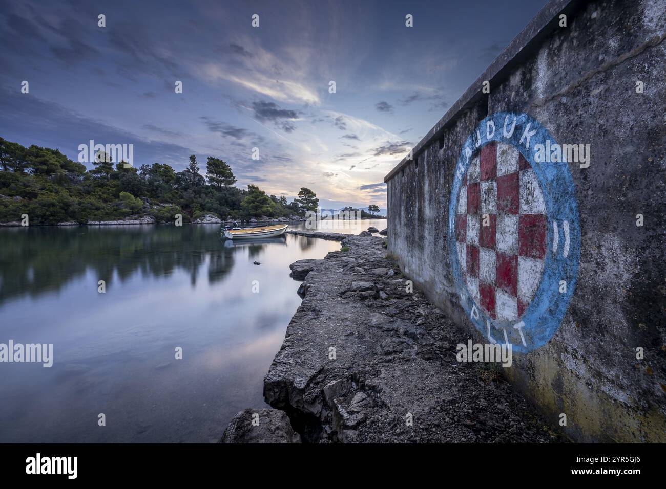 Graffiti auf einer Steinmauer mit Blick auf das Meer mit einem Boot bei Sonnenaufgang, Korcula, Kroatien, Europa Stockfoto