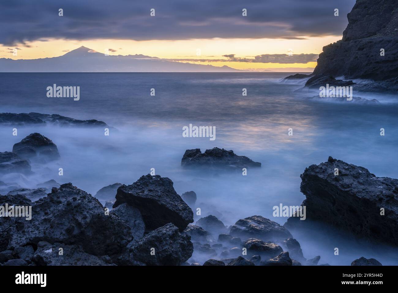 Vor Sonnenaufgang am Strand von San Marcos. Felsen und Meer. Teneriffa und der Teide im Hintergrund. Lange Belichtung. La Gomera, Kanarische Inseln, Spanien, E Stockfoto