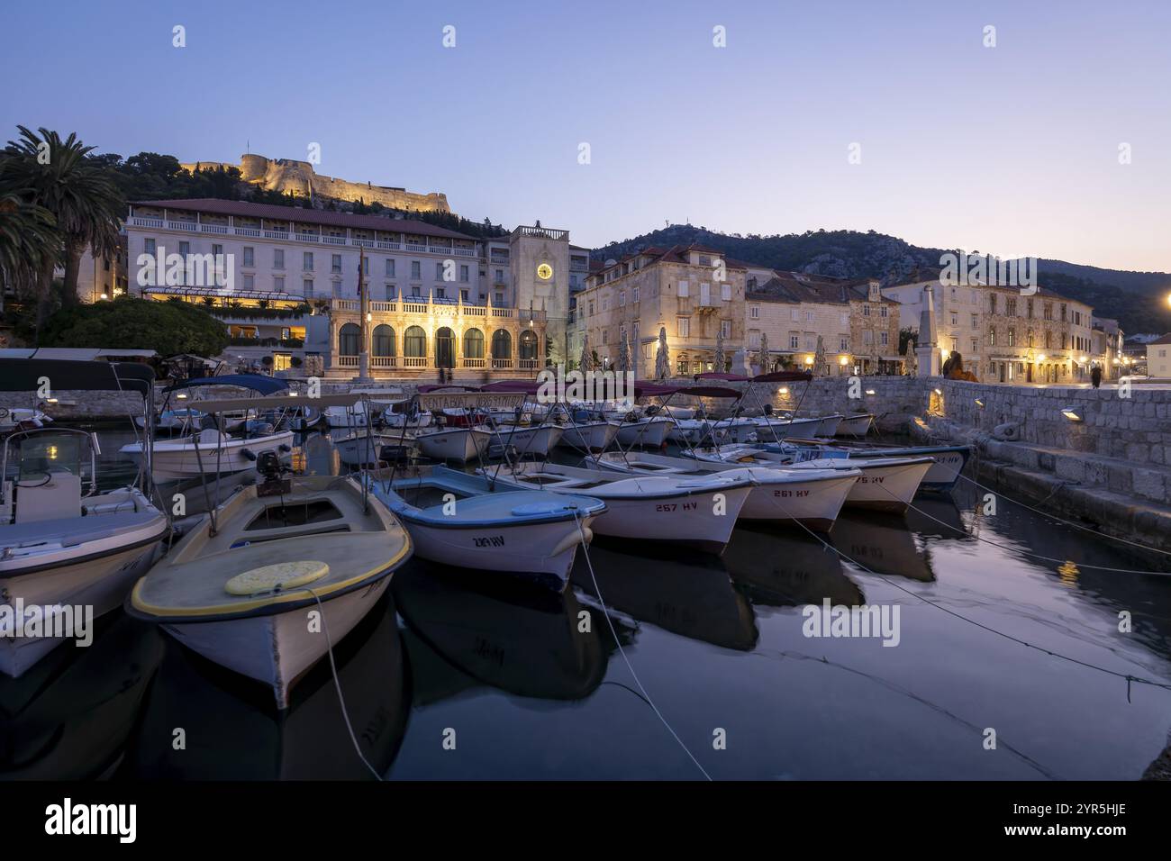 Beleuchteter Hafen bei Sonnenaufgang mit Booten und historischen Gebäuden, Hvar, Kroatien, Europa Stockfoto