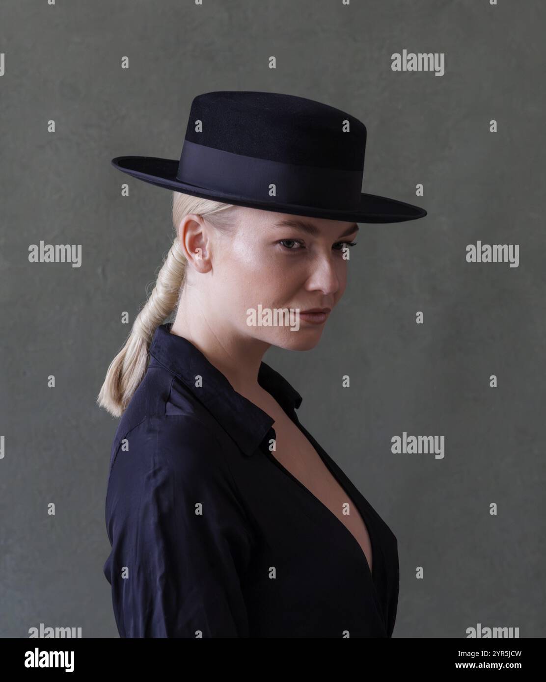 Frau in schwarzer Kleidung und Hut, die im Seitenprofil vor grünem Hintergrund schaut, Fotoshooting Stockfoto