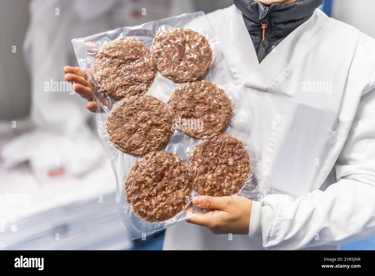 Unerkennbare Arbeiterin, die ein Paket frischer, vakuumversiegelter Hamburger in einer Fabrik hält Stockfoto