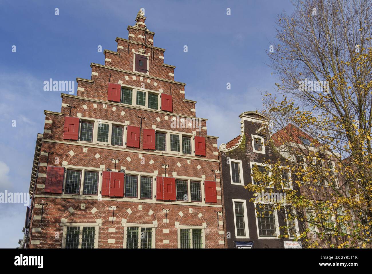 Backsteingebäude mit Stufengiebel und roten Rollläden unter blauem Himmel, Amsterdam, Niederlande Stockfoto