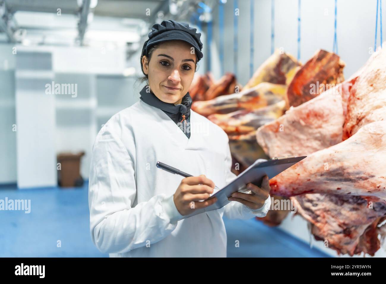 Metzgerinnen, die Qualitätsberichte schreiben und Notizen in einem Klemmbrett in einer Fleischverarbeitungsfabrik schreiben Stockfoto