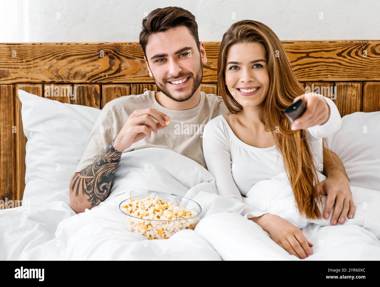 Unterhaltung am Abend. Lächelnder Mann isst Popcorn, Frau drückt Knopf auf der Fernbedienung Stockfoto
