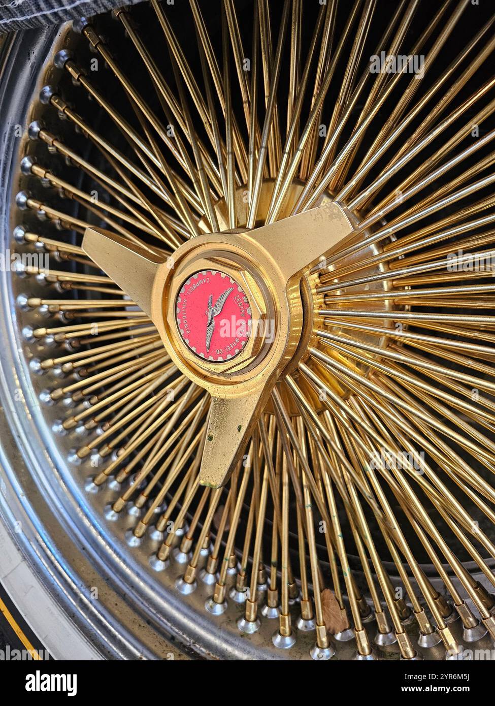 Detaillierte Ansicht eines Oldtimerrads mit goldenen Speichen und einem zentralen Emblem, der Eleganz und klassisches Kfz-Handwerk unterstreicht. Stockfoto