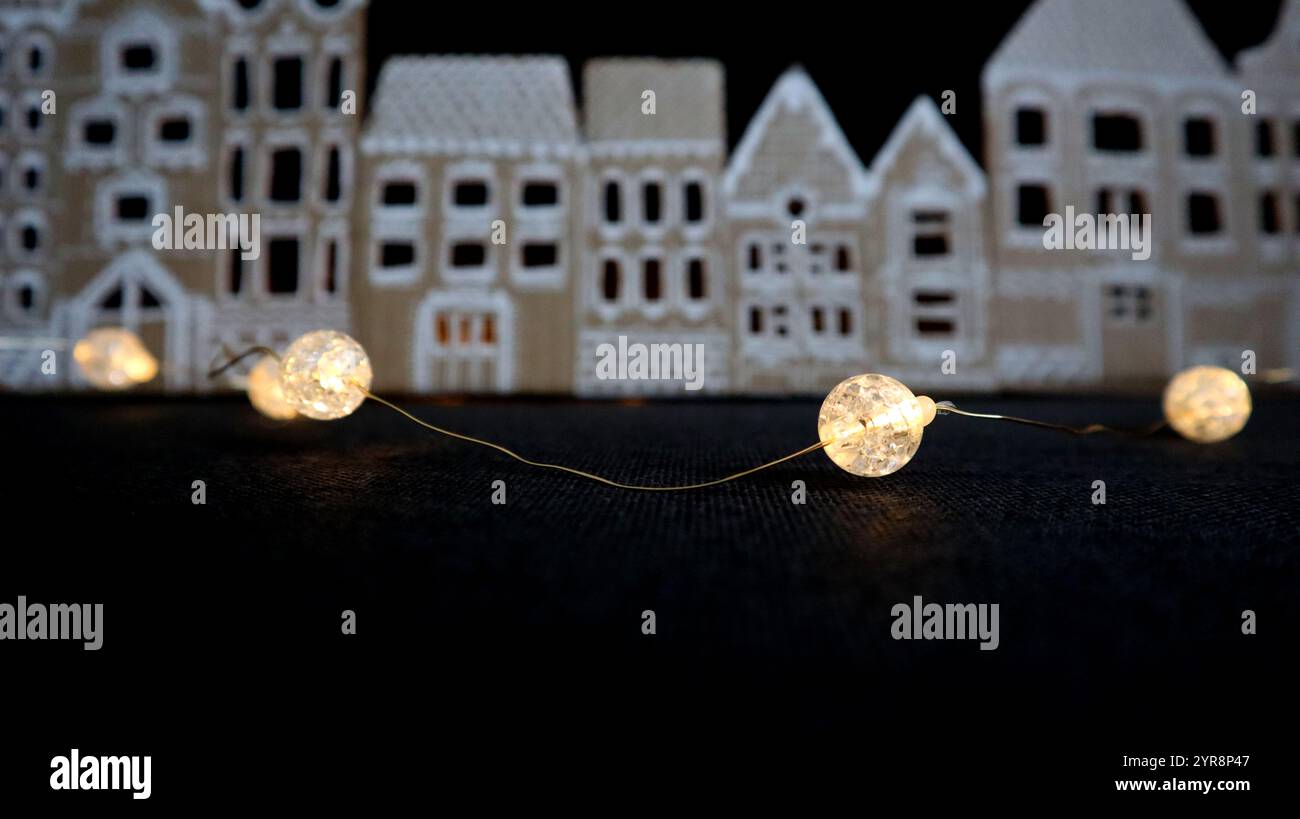 Girlanden-Kugeln mit Diamantstruktur. Runde Form. Gelbes warmes Licht. Verbindungen mit dünnem Pfeil. Zum Hintergrund Unschärfepanorama alter Häuser. Ha Stockfoto
