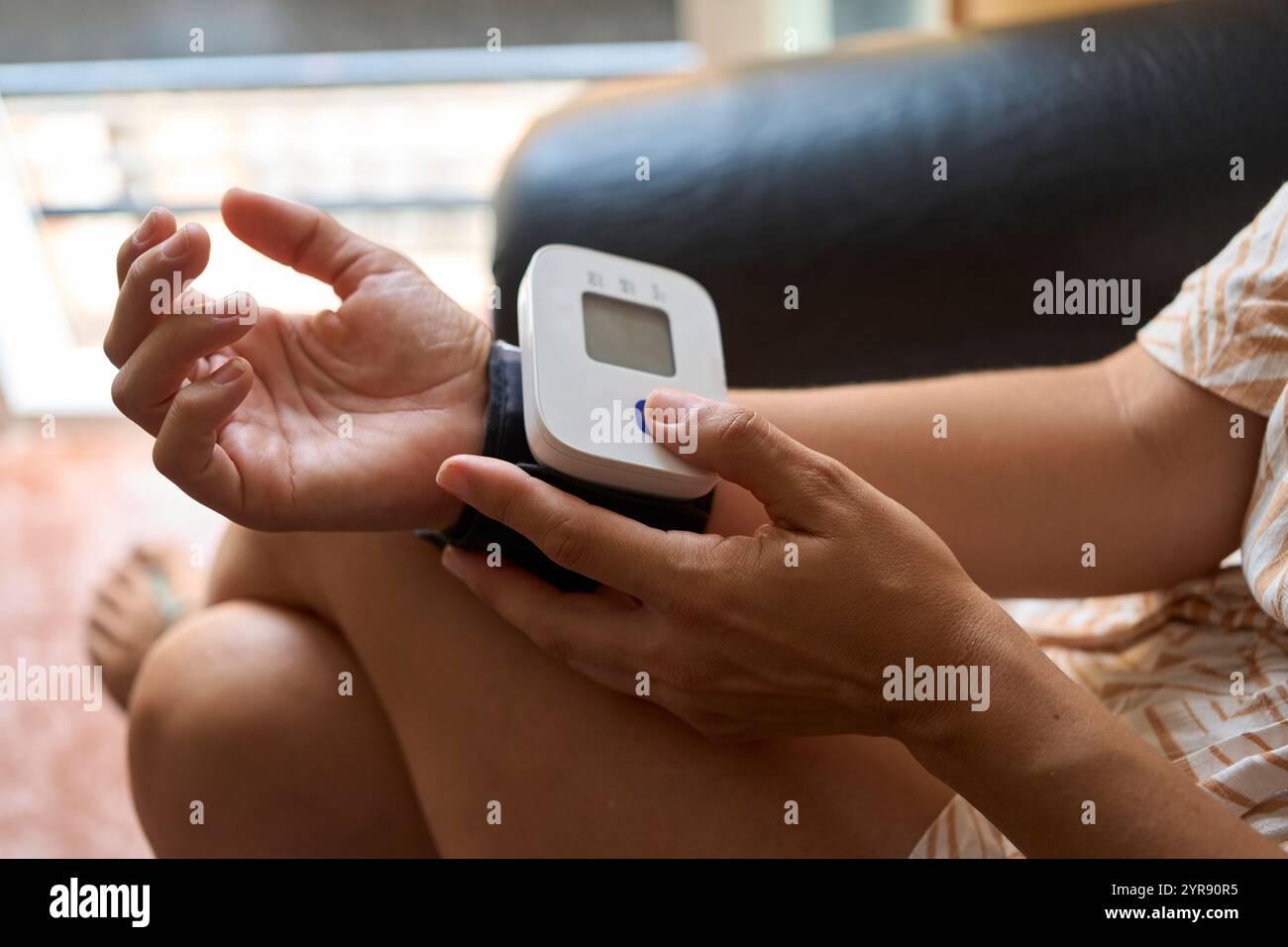 Frau mit einem tragbaren Blutdruckmessgerät am Handgelenk, die ihren Gesundheitszustand in einer häuslichen Umgebung überprüft Stockfoto