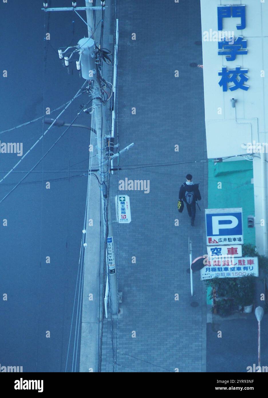 Ein Fußgänger läuft auf dem Bürgersteig unter einer Plakatwand mit japanischen Schriftzeichen, die bedeuten: Der beste Weg, einen Job zu bekommen Stockfoto