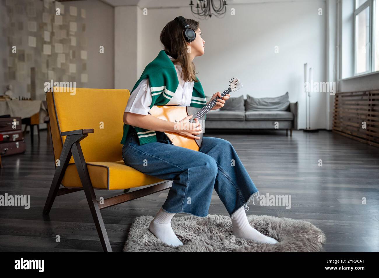 Eine fokussierte Frau spielt Balalaika, fühlt Musik zu Hause über Kopfhörer, übt das Zupfen von Saiten Stockfoto