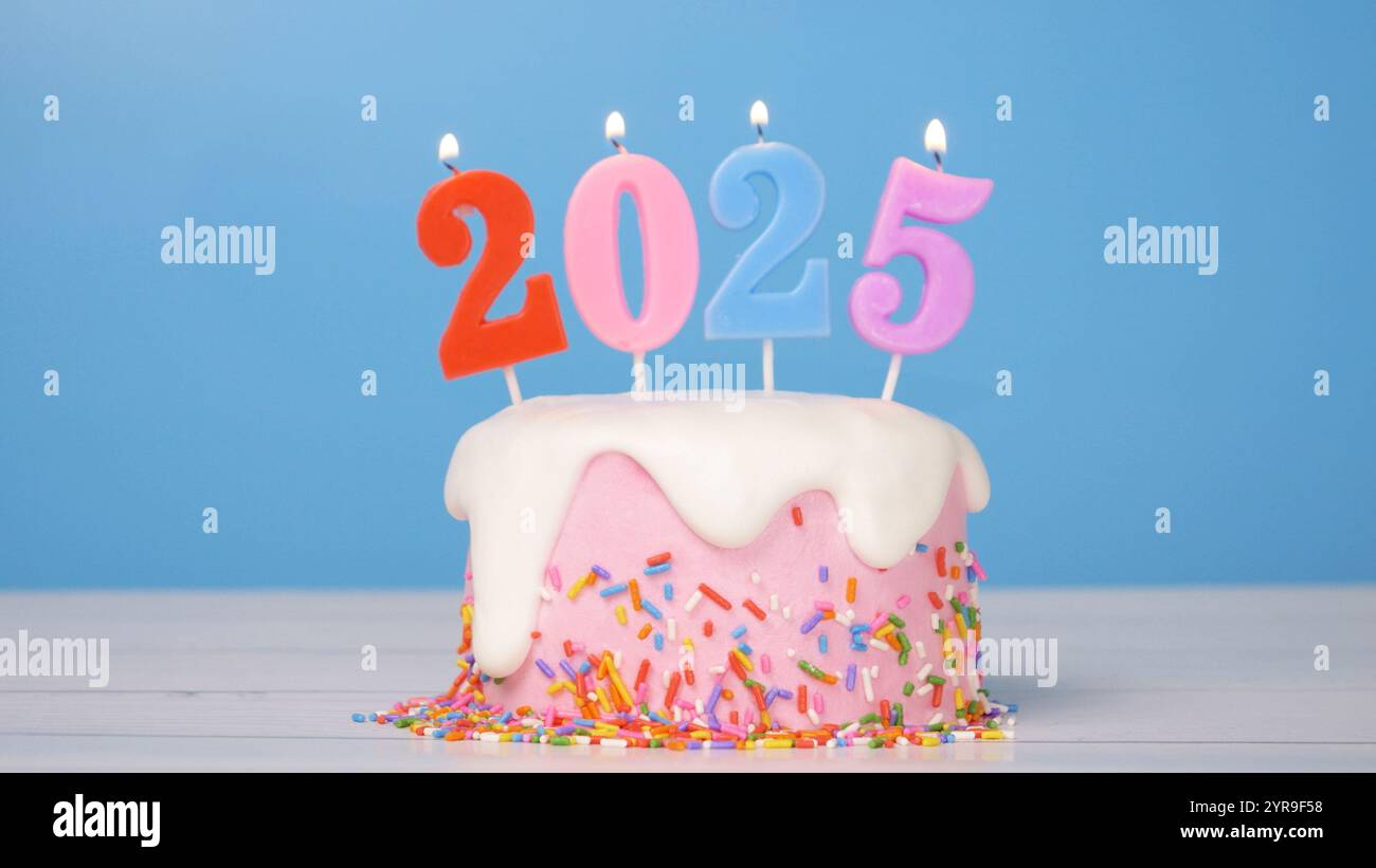 Happy New Year 2025, süßer Kuchen mit bunter Kerze Nummer 2025 für Neujahrsfeier wurde angezündet. Flamme am Kerzenwickel mit blauem Hintergrund Stockfoto