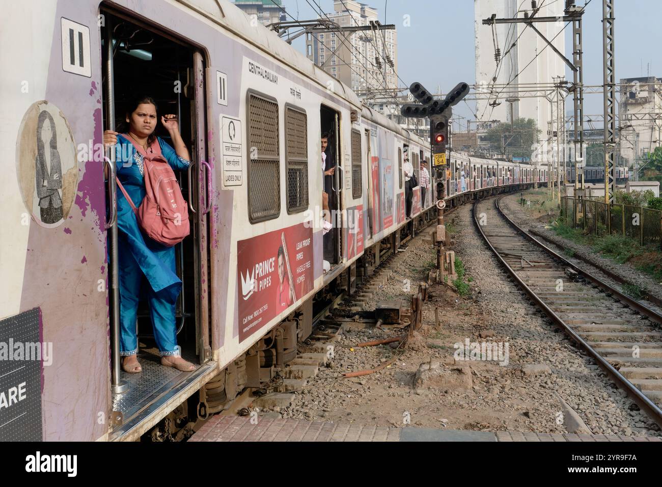 Mumbai, Indien: Eine weibliche Fahrgastin steht prekär an der offenen Tür eines Vorortzuges, der in den Chhatrapati Shivaji Maharaj Terminus fährt Stockfoto