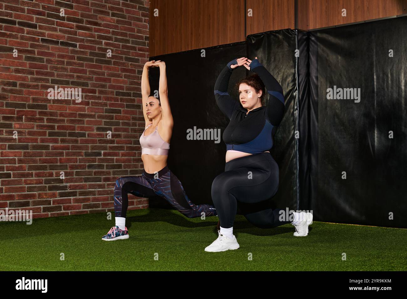 In einem modernen Fitnessraum nehmen zwei Frauen Ausfallschritte in Anspruch und zeigen Teamwork im Fitnessbereich. Stockfoto