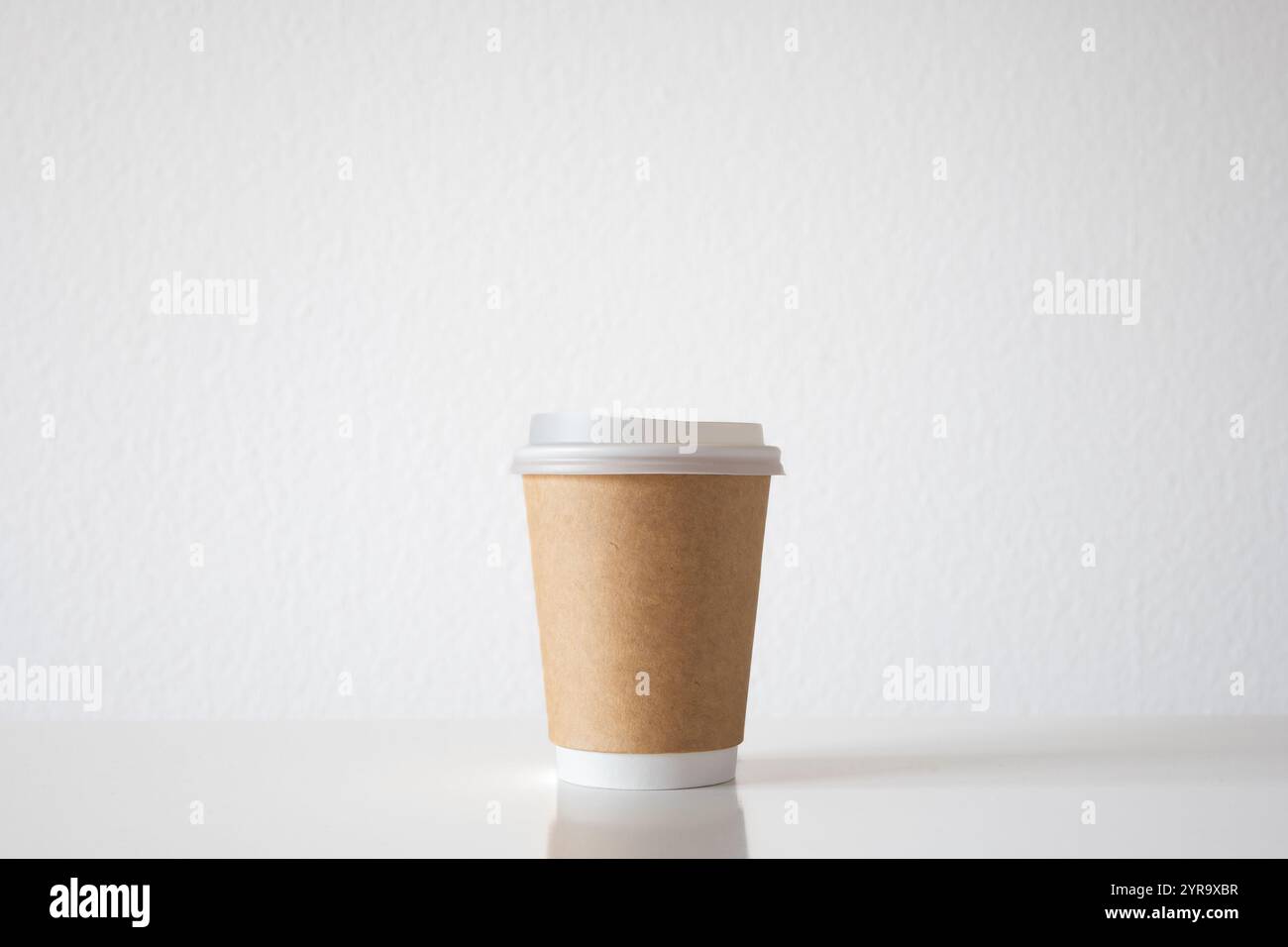 Leere, generische Kaffeetasse zum Mitnehmen aus Kunststoff mit brauner Papierverpackung, isoliert auf weiß. Nahaufnahme, kein Branding, keine Logos, keine Leute. Stockfoto