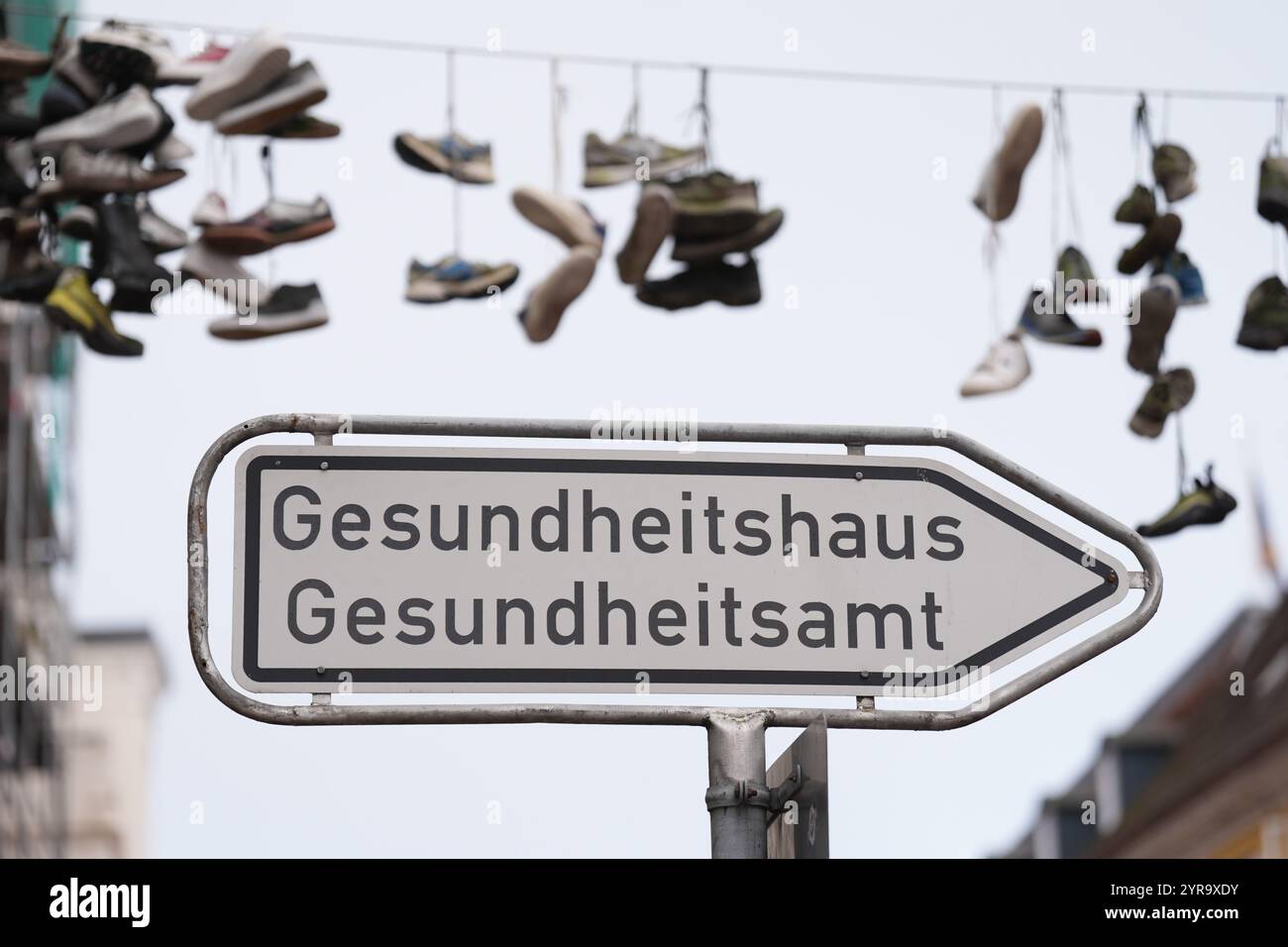 Flensburg, Deutschland. Dezember 2024. Schuhe hängen an einem Drahtseil oberhalb der Norderstraße. Im Vordergrund ist ein Wegweiser mit den Worten Gesundheitshaus und Gesundheitsamt zu sehen. Quelle: Marcus Brandt/dpa/Alamy Live News Stockfoto