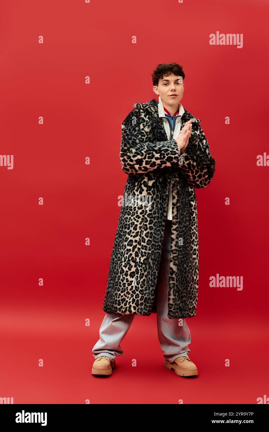 Ein hübscher Mann in einem auffälligen Mantel mit Leopardenmuster steht stilvoll in einem auffälligen roten Setting. Stockfoto