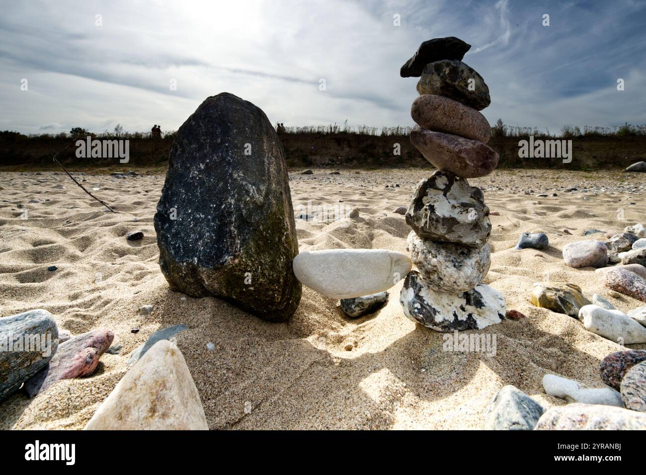 Weißer ausgeglichener Stein zwischen angeordneten Natursteinpfählen am Sandstrand der Ostsee, der Harmonie und einen ruhigen und ausgewogenen Lebensstil darstellt Stockfoto