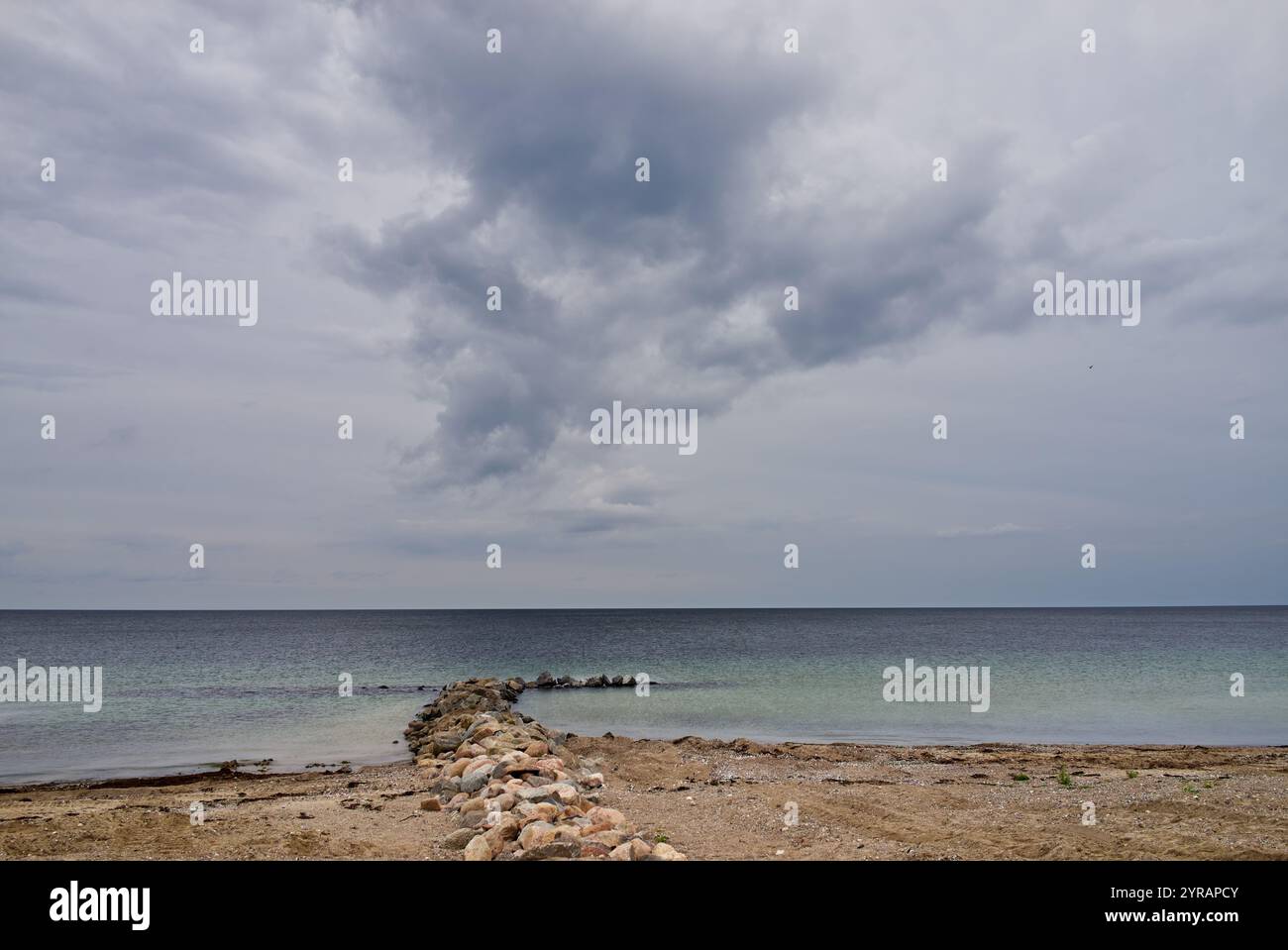 Blick vom Strand an der Ostsee bei bewölktem Wetter mit einer riesigen dramatischen Wolke, die am Himmel über einer Steingroyne hängt (Mitte) Stockfoto