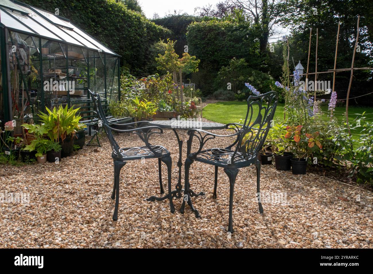 Gartenszene, Stühle und Tisch mit Gewächshaus in einem sonnigen Devon Garten, Blumen und Sträucher Stockfoto