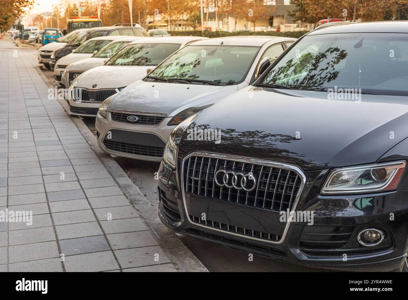 Eine Reihe von Autos, die vor dem Weg auf der Straße geparkt sind. Neue und alte Autos parkten am Straßenrand. Reise- und Geschäftskonzept. Straßenansicht, s Stockfoto Eine Reihe von Autos, die vor dem Weg auf der Straße geparkt sind. Neue und alte Autos parkten am Straßenrand. Reise- und Geschäftskonzept. Straßenansicht, s Stockfoto