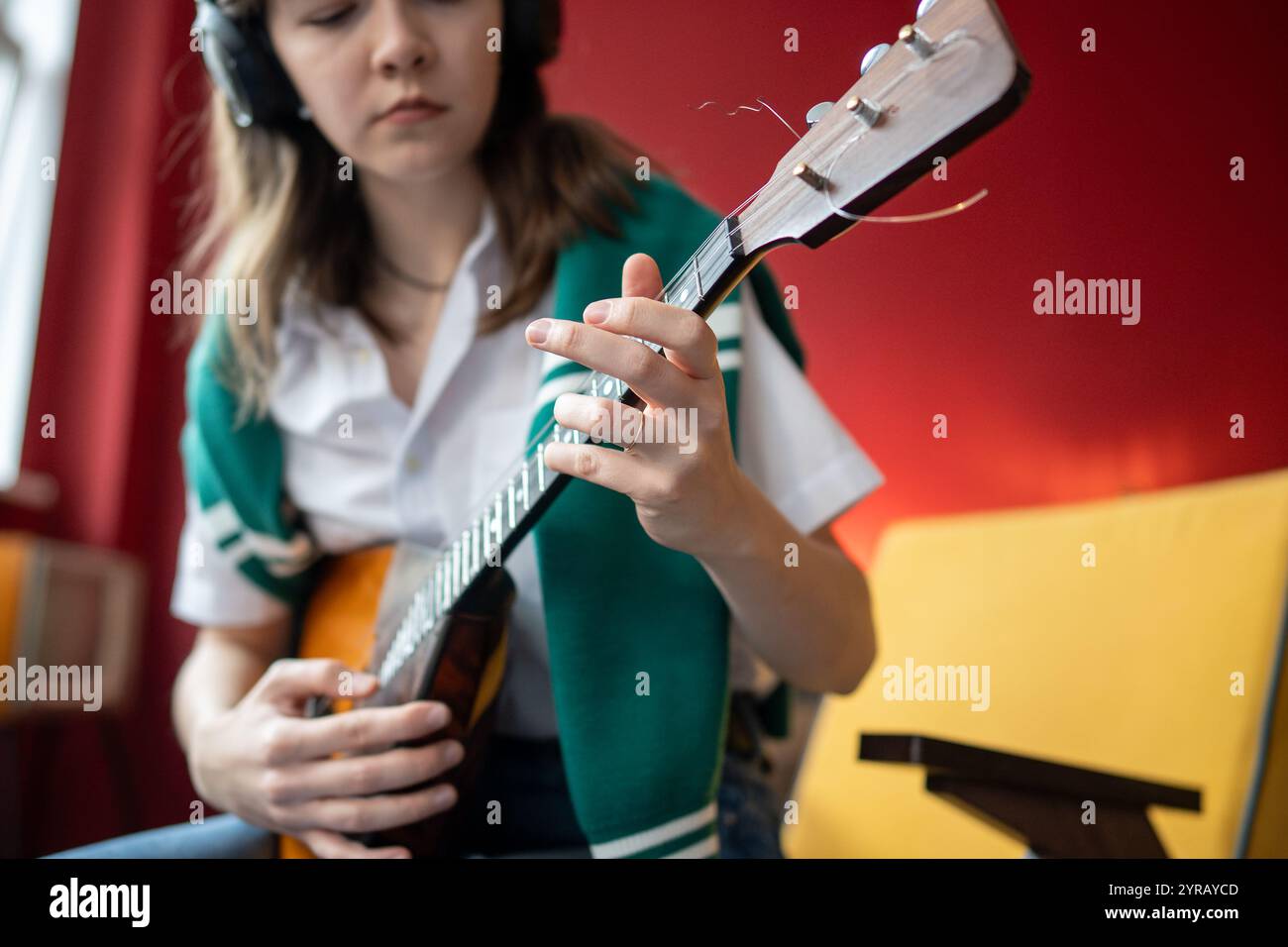Frau übt Balalaika-Akkorde mit Kopfhörern, während sie im Rhythmus spielt. Musikübungen zu Hause Stockfoto
