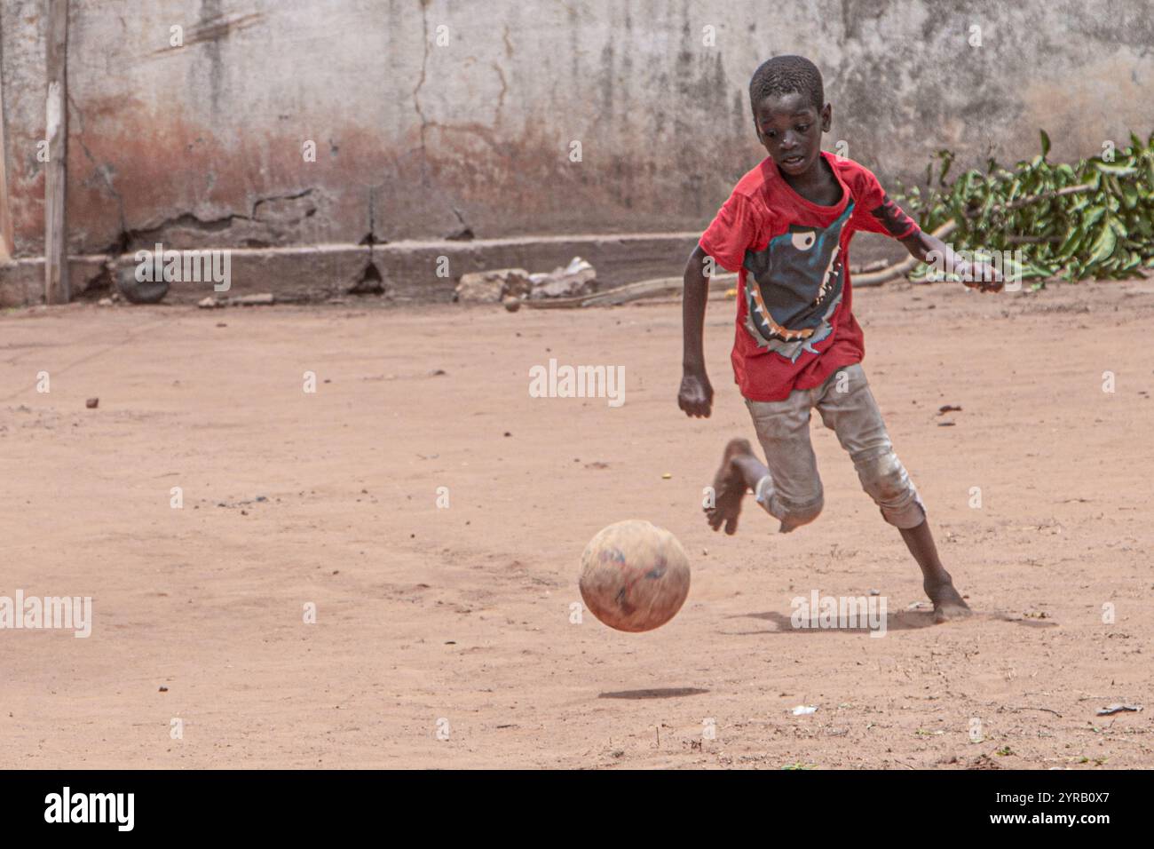 Togolese Boy spielt Fußball auf einem staubigen Feld in Togo und hält Freude und Leidenschaft für Fußball fest Stockfoto