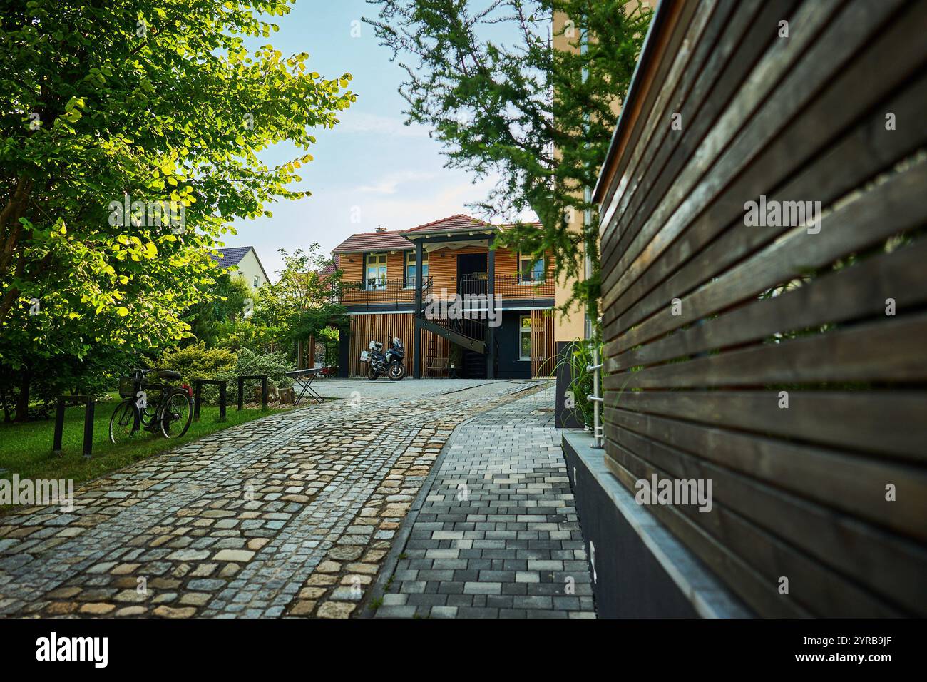 Eine charmante Wohngegend in Neuzelle, Deutschland, mit einem Holzhaus mit rotem Ziegeldach, umgeben von Grün und einer kopfsteingepflasterten Zufahrt. Stockfoto
