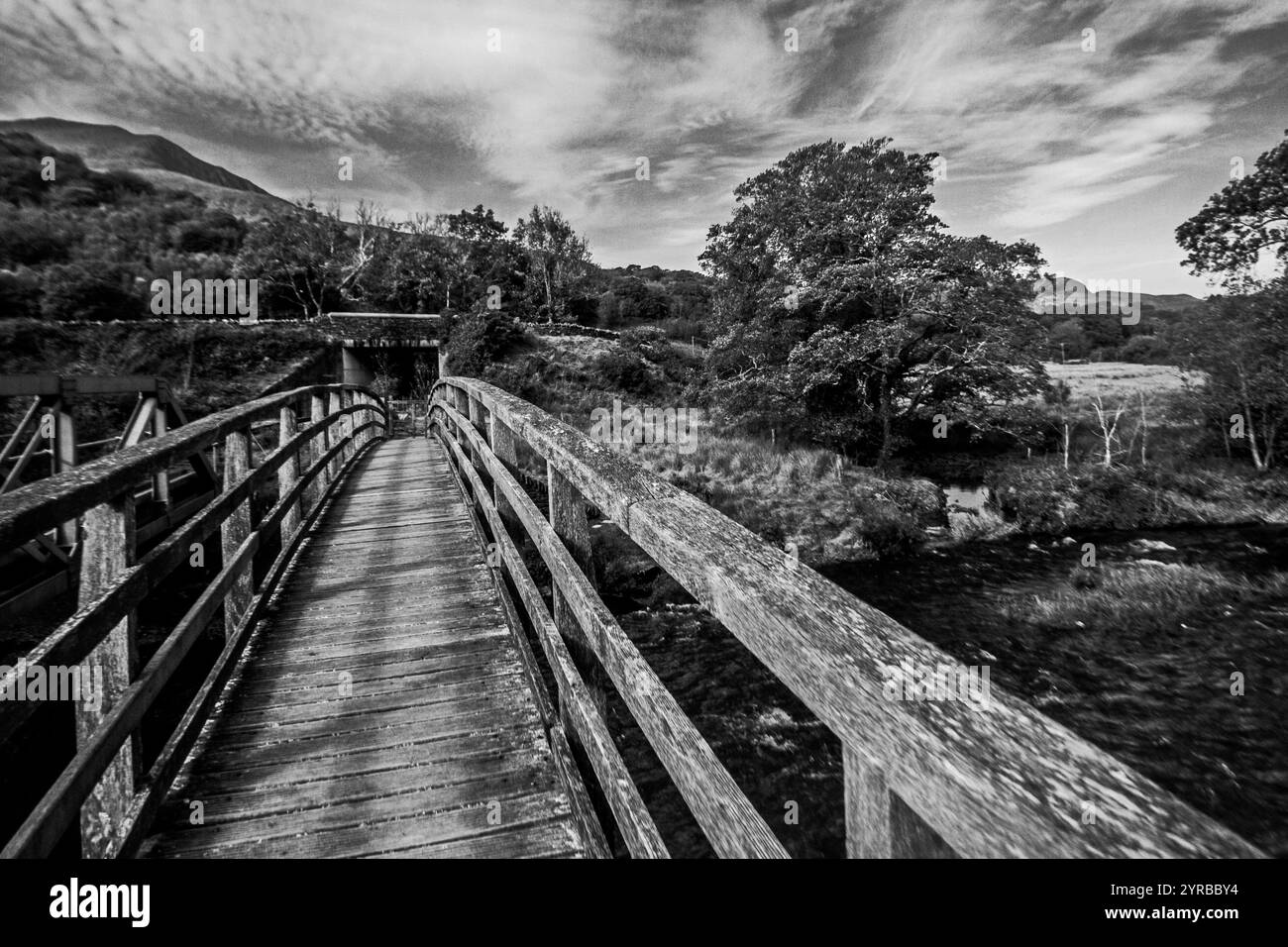 Dramatische Schwarzweiß-Aussicht entlang einer verwitterten hölzernen Wanderbrücke über den Fluss Glaslyn im Eryri-Nationalpark in Wales Stockfoto