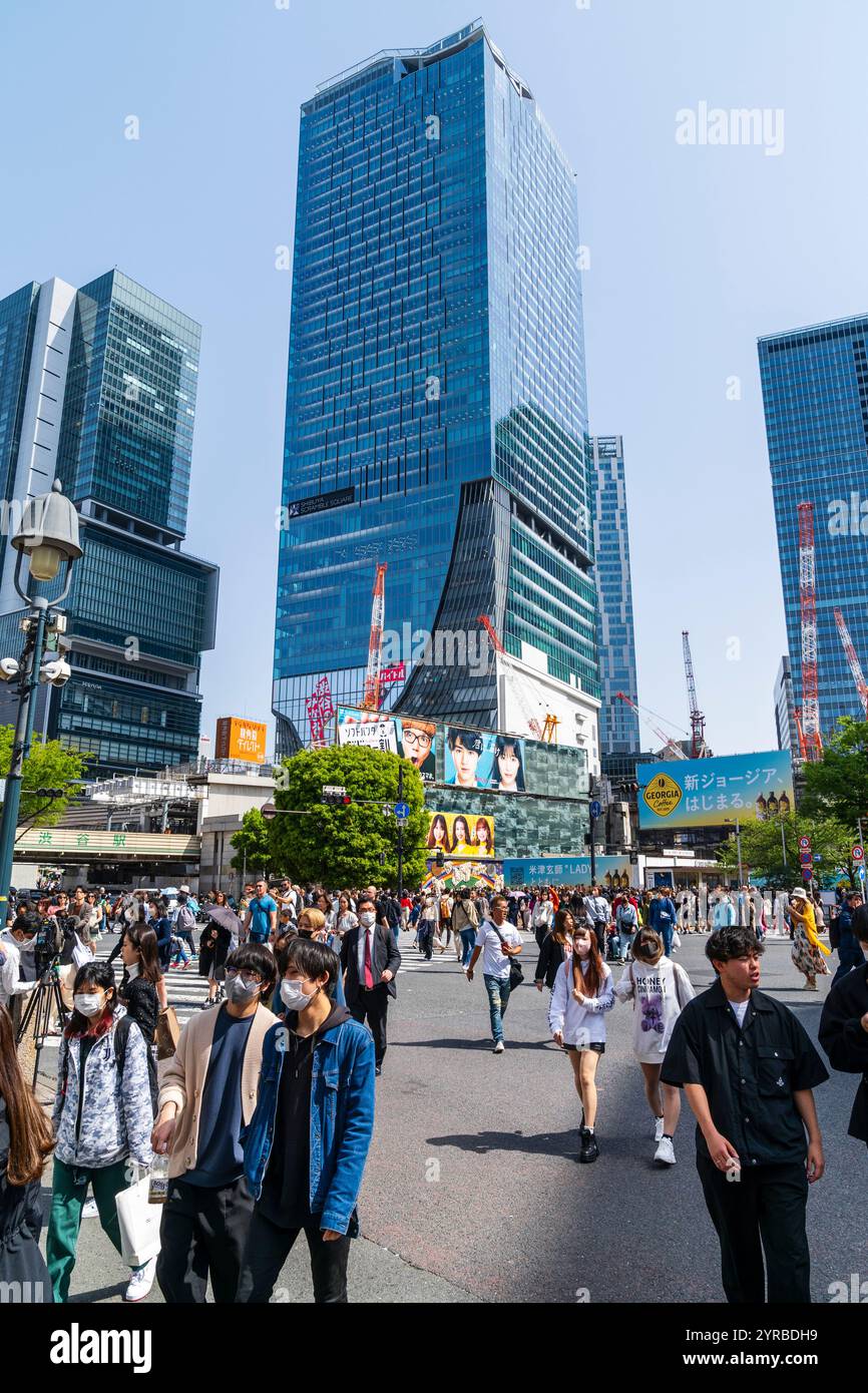 Shibuya Scramble Crossing Gebäude mit Blick auf Menschenmassen, die in der hellen Frühlingssonne über die berühmte Fußgängerüberquerung laufen. Stockfoto