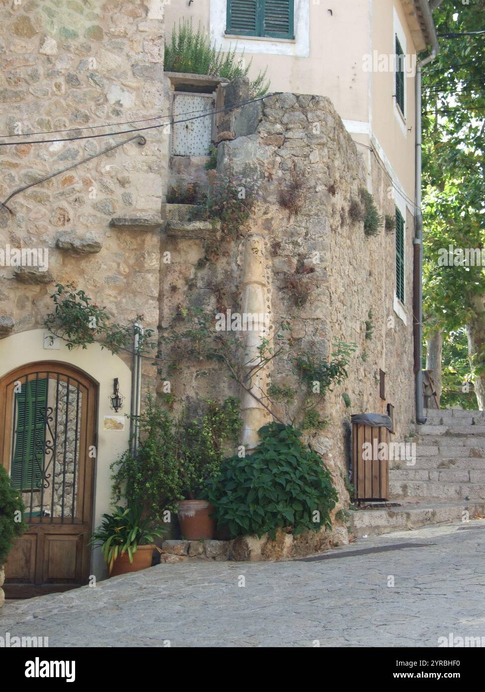 Eine malerische Ecke eines Dorfes zeigt rustikale Steinarchitektur mit üppigem Grün, Topfpflanzen und einer ruhigen Treppe, die ins Herz führt Stockfoto