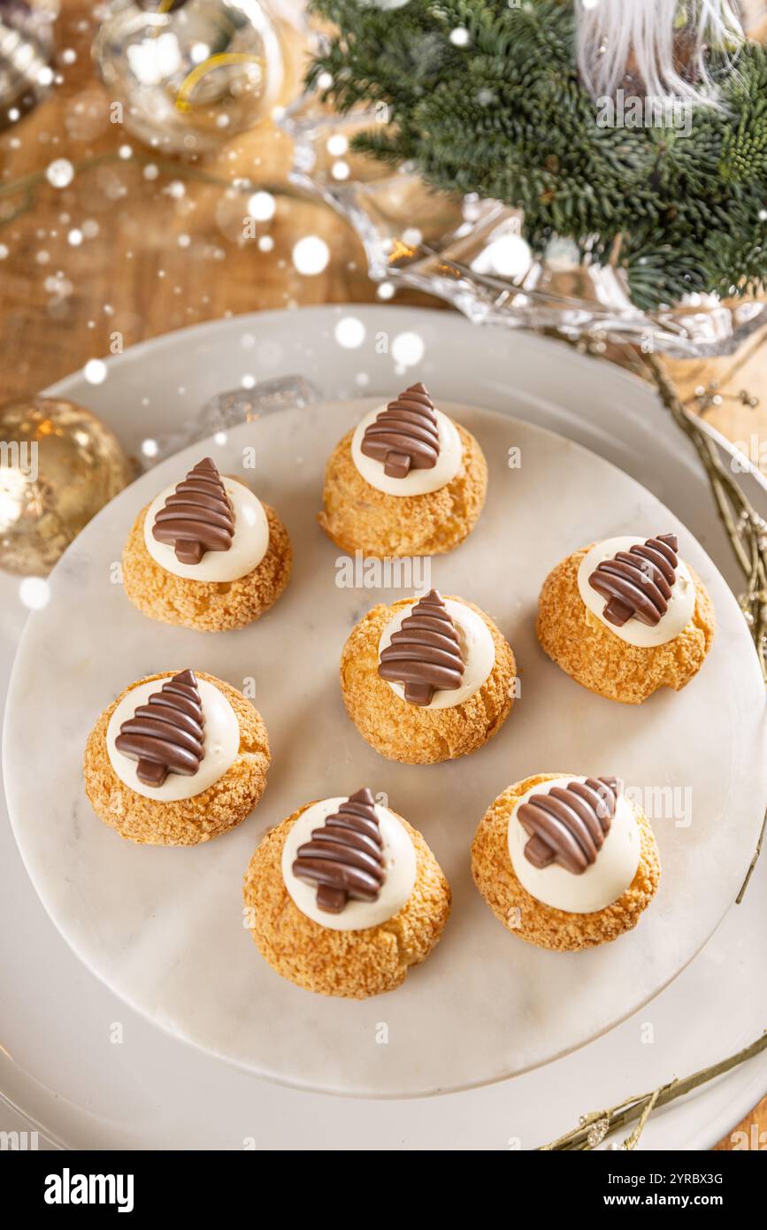 Weihnachtscremepuffs, dekoriert mit Schokoladenbäumen auf Marmorkuchenständer Stockfoto