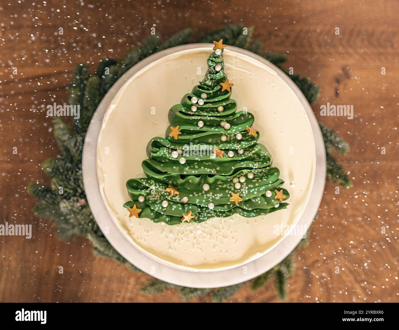 Köstlicher Weihnachtsbaumkuchen, dekoriert mit goldenen Sternen und weißen Perlen, fallender Schnee Stockfoto