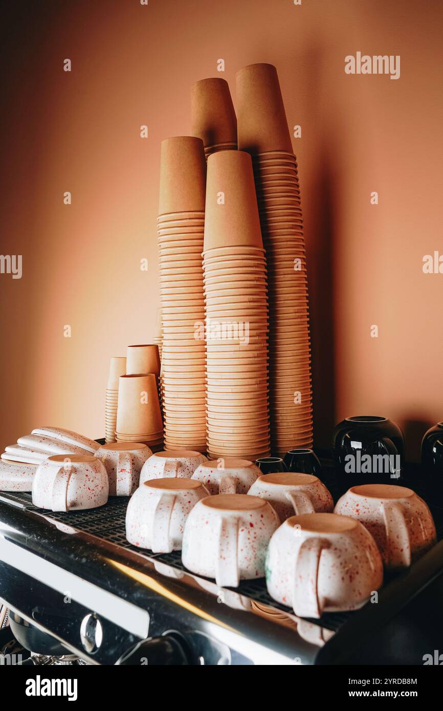 Gestapelte Pappbecher säumen die Oberseite der Kaffeemaschine, deren umweltfreundliches Design Stil und Nachhaltigkeit perfekt verbindet. Stockfoto